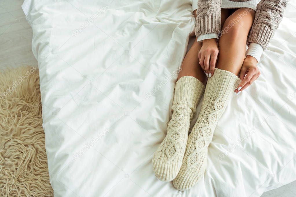 cropped view of woman taking on knitted socks at morning 