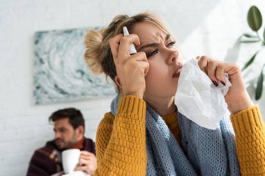 Burun spreyi ve peçetelerle baş ağrısı çeken hasta bir kadın.