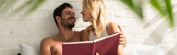 smiling couple hugging and reading book together in bed in the morning 