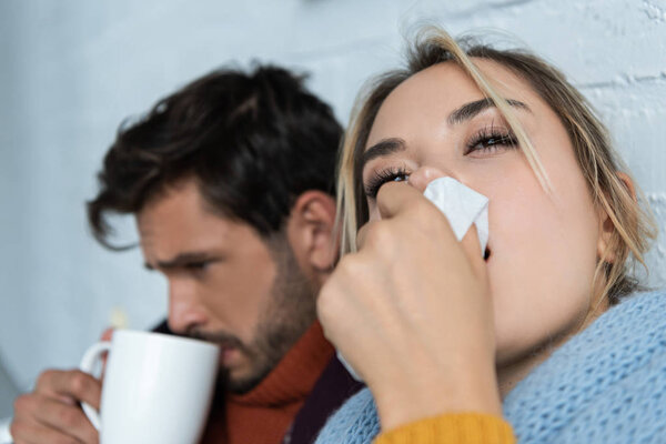 sick man with hot drink and woman with napkin having runny nose
