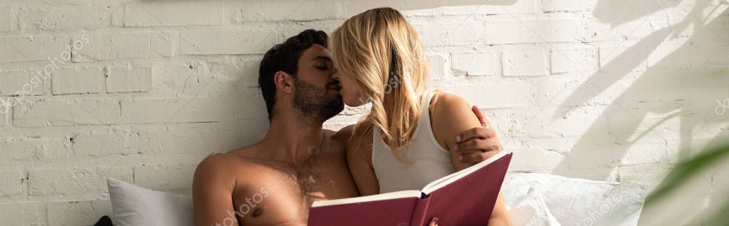 tender couple kissing and holding book in bed in the morning 