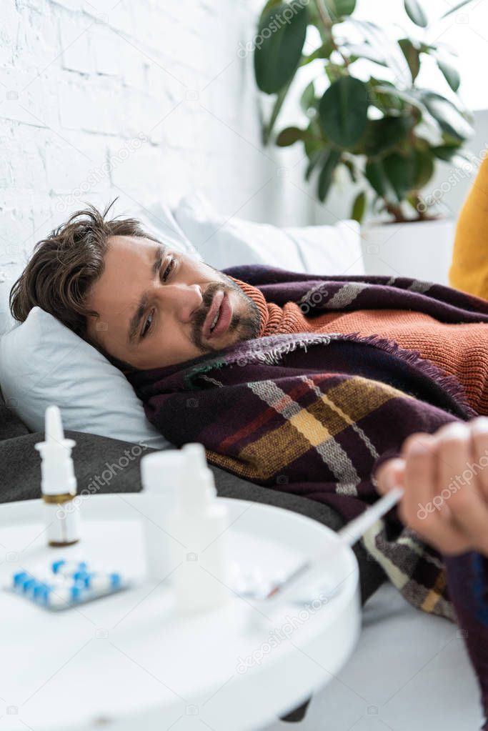 Sick man lying in bed with medicines on table at home