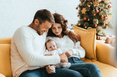 Mutlu ebeveynler sarı koltukta otururken sevimli bir bebek tutuyorlar.