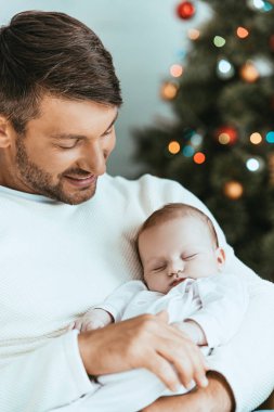 Mutlu baba Noel ağacının yanında uyuyan bebeği tutuyor.