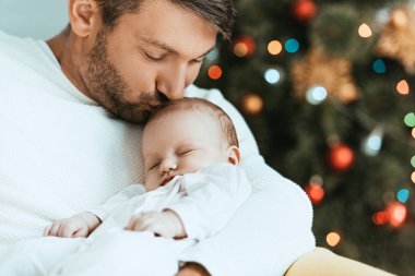 Mutlu baba kucağında uyuyan bebeği öpüyor. 