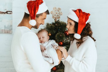Mutlu kadın gülümseyen kocaya bakıyor. Küçük kızını Noel ağacının yanında tutuyor.
