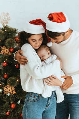 Mutlu baba karısına sarılıyor Noel ağacının yanında sevimli bir bebek tutuyor.