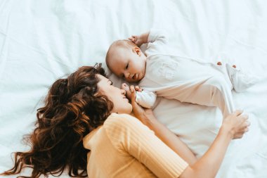Annenin beyaz bir yatakta yatarken küçük tatlı kızının bacağına dokunuşunun en üst görüntüsü.