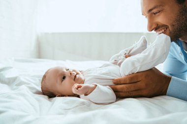 Mutlu baba beyaz yatağa uzanmış tatlı küçük kızına dokunuyor.