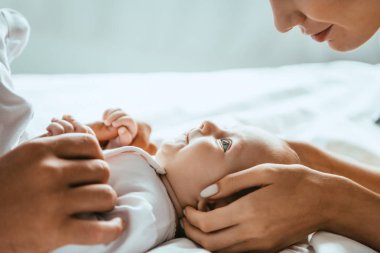 Anne ve babanın yatağın üzerinde uzanan bebeğe nazikçe dokunuşları.