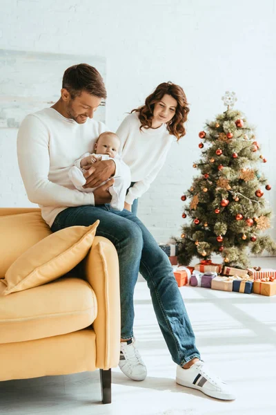 Happy Woman Standing Christmas Tree Looking Husband Holding Cute Baby — Stock Photo, Image