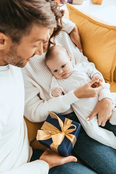 Baba, küçük sevimli kızına hediye paketi sunuyor. Annenin ellerinde oturuyor.