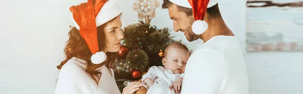 幸せな女性は笑顔の夫を見ているクリスマスツリーの近くに娘を保持 — ストック写真