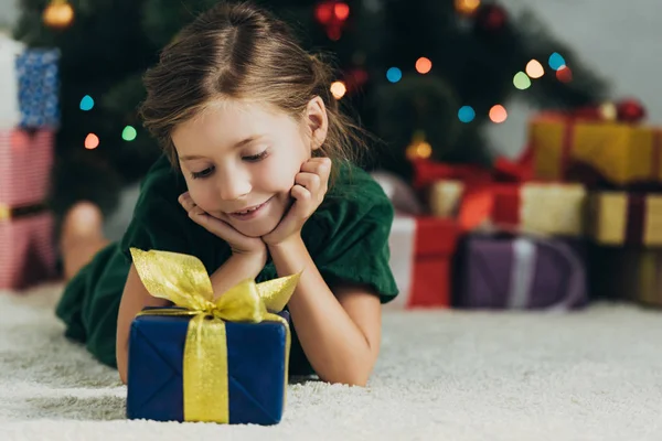 快乐的孩子躺在圣诞树旁的地板上 看着礼品盒 — 图库照片