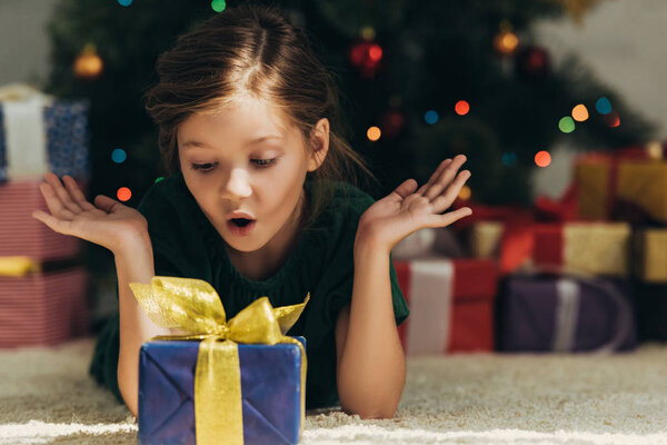 surprised child lying on floor, looking at gift box and showing wow gesture