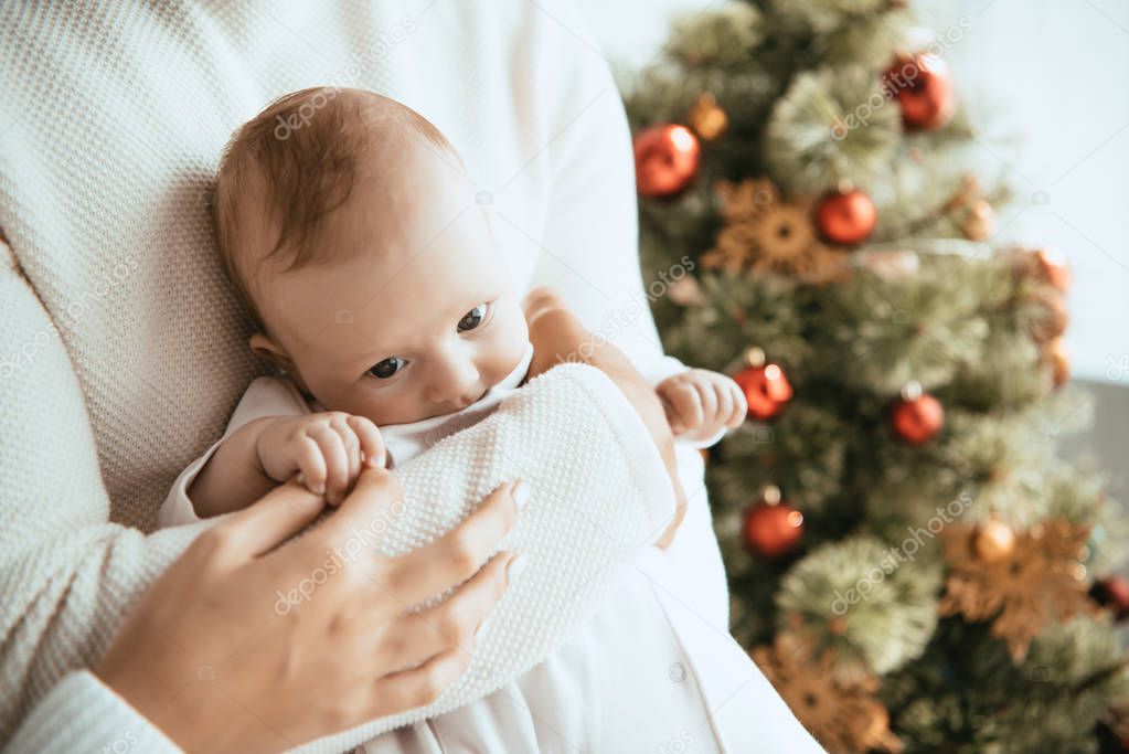 cropped view of father holding adorable baby near christmas tree