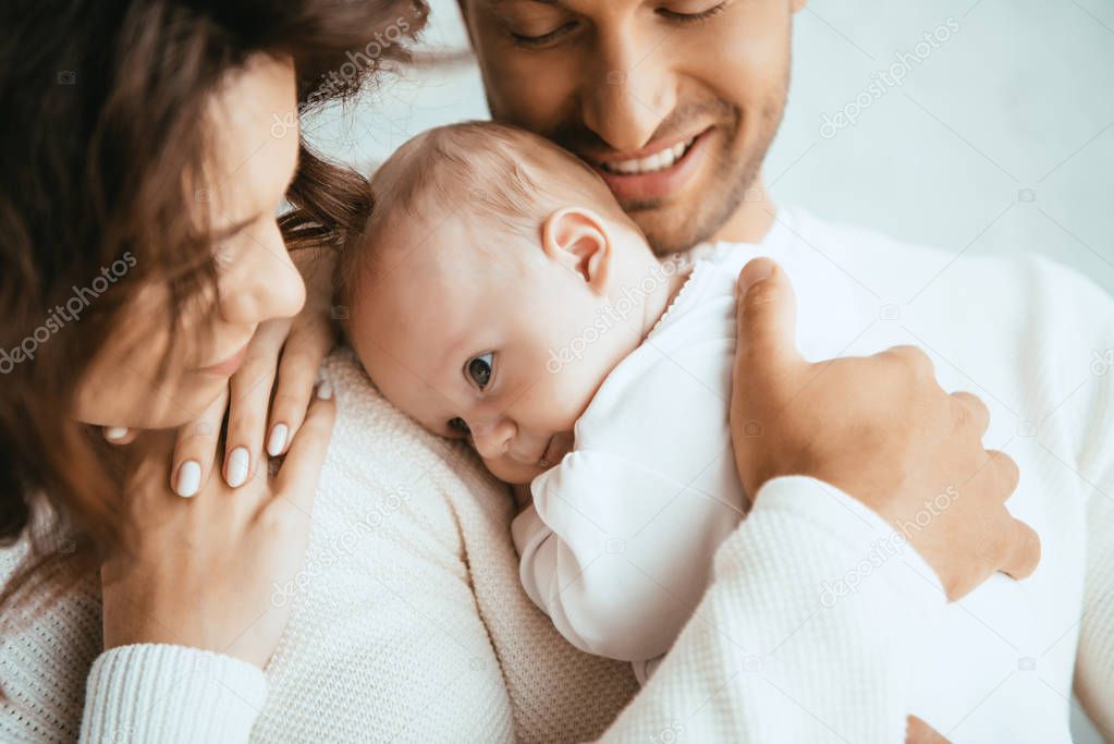 cropped view of happy man holding adorable baby near smiling wife