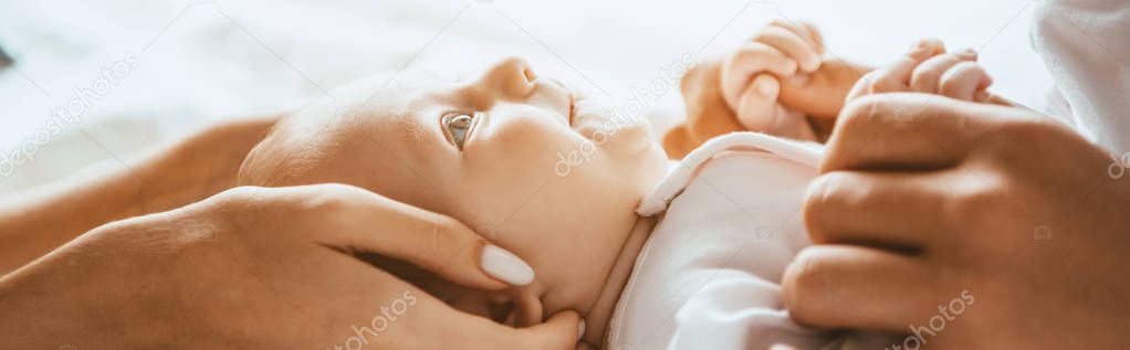 cropped view of mom and dad gently touching infant lying on bedding, panoramic shot