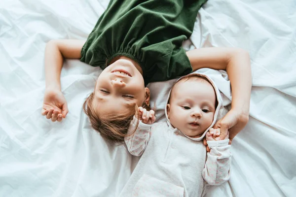妹の近くの白い寝具に寝そべっている子供の笑顔のトップビュー — ストック写真