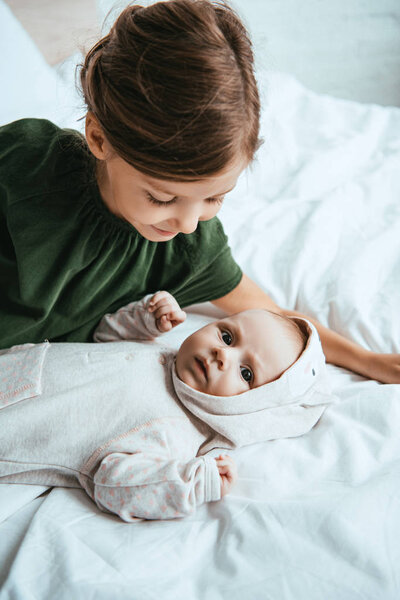 adorable child looking at cute little sister lying on white bedding 