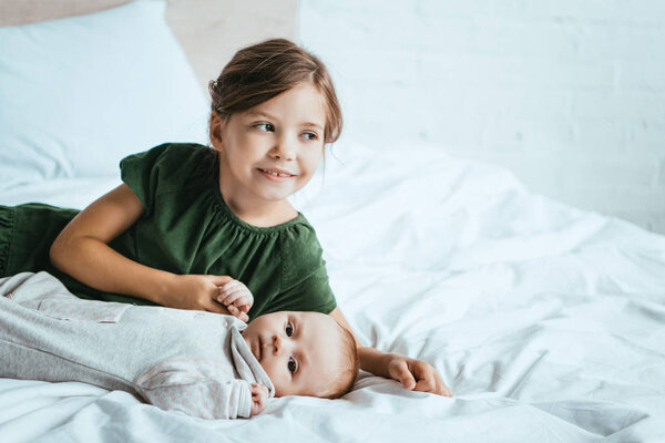 smiling child holding hand of little sister lying on white bedding