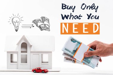 cropped view of man holding money near house and car models, buy only what you need lettering isolated on white clipart