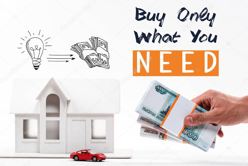 cropped view of man holding money near house and car models, buy only what you need lettering isolated on white