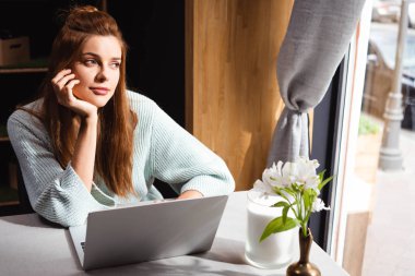 Kafede dizüstü bilgisayar kullanan düşünceli kızıl saçlı kadın.