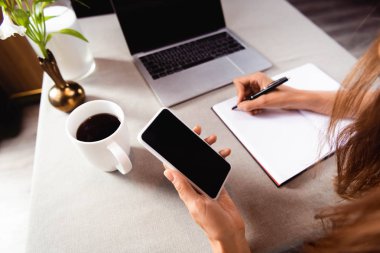 Kafede not defteri, akıllı telefon ve dizüstü bilgisayarla çalışan kadın görüntüsü