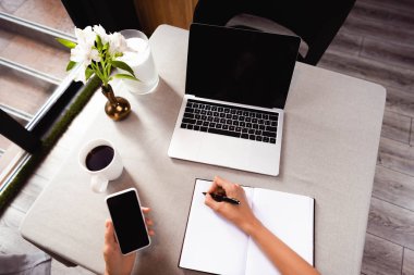 Kafede not defteri, akıllı telefon ve dizüstü bilgisayarla çalışan bir kadın görüntüsü 