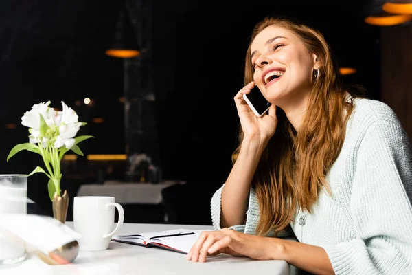 Skrattande Kvinna Talar Smartphone Café Med Anteckningsblock Och Kopp Kaffe — Stockfoto