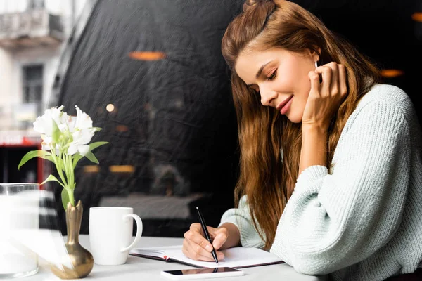 Aantrekkelijk Gelukkig Vrouw Schrijven Notitieblok Cafe Met Smartphone Kopje Koffie — Stockfoto