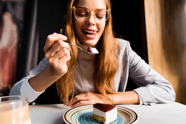 カフェでコーヒーとおいしいケーキを食べながら舌を出している魅力的な女の子 — ストック写真