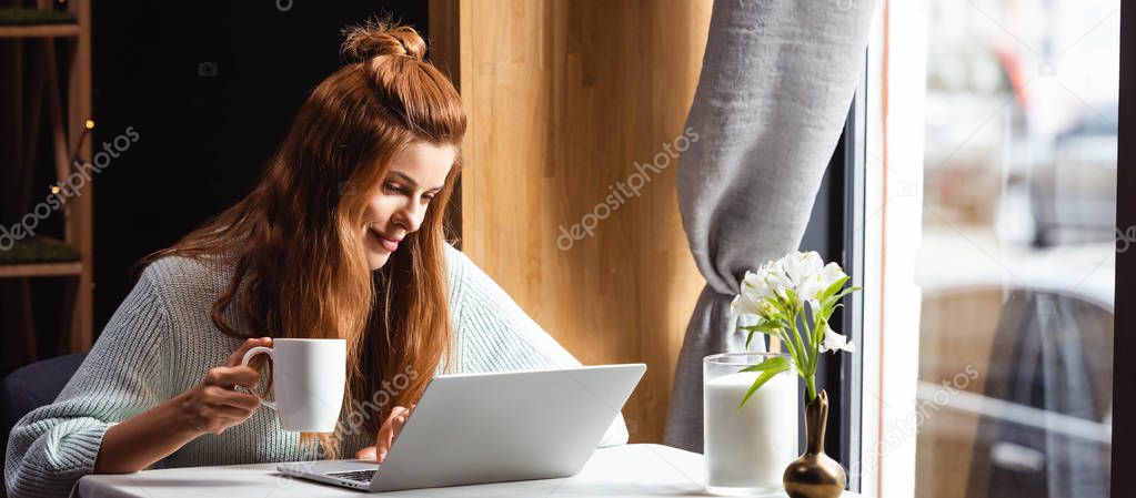 beautiful smiling woman with cup of coffee using laptop in cafe