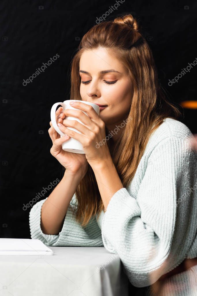 tender woman with closed eyes holding cup of coffee in cafe 