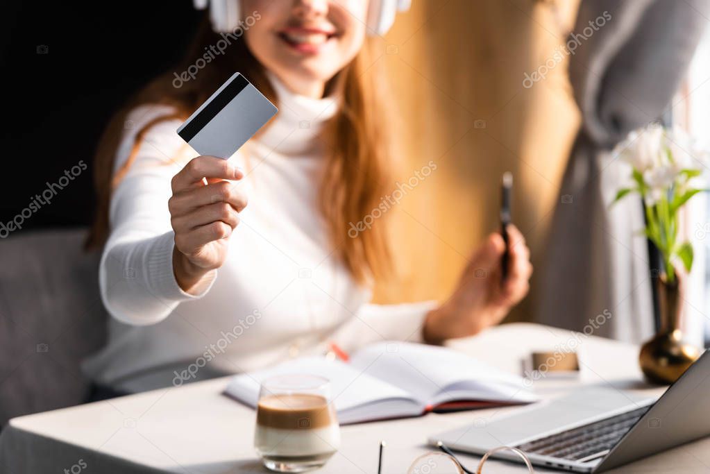 cropped view of woman in headphones paying with credit card in cafe, selective focus