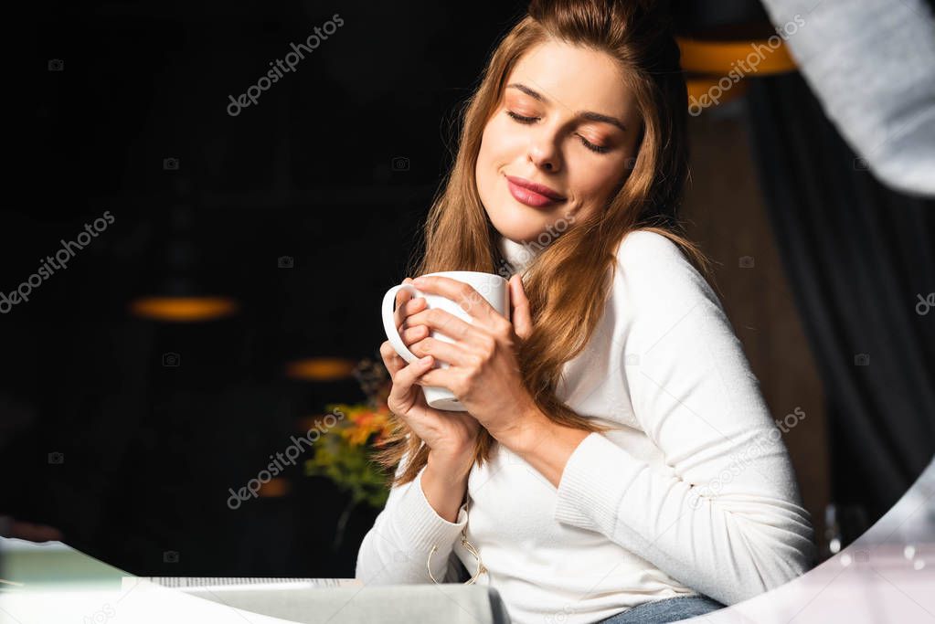dreamy woman with closed eyes holding cup of coffee in cafe 
