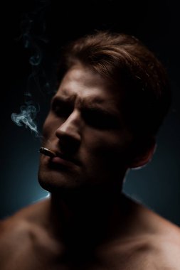 Yakışıklı seksi adam karanlık odada sigara içiyor.