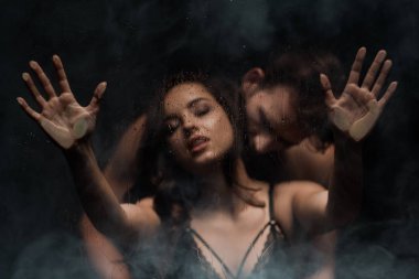 Islak camın arkasında sarılan baştan çıkarıcı genç çift.