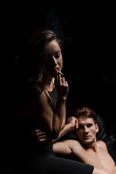 迷人的年轻夫妇坐在黑暗的房间里的沙发上 而女人则吸烟 — 图库照片