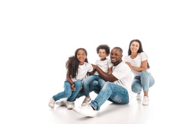 Beyaz arka planda otururken kameraya gülümseyen mutlu Afro-Amerikan ailesi