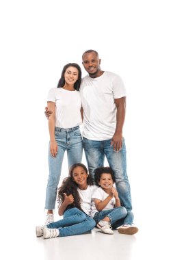 happy african american man hugging wife while standing near chidren sitting on white background clipart