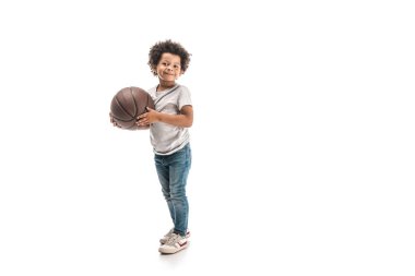 Amerikalı neşeli Afro-Amerikan çocuk basketbol topu tutuyor ve beyaz arka planda kameraya gülümsüyor.