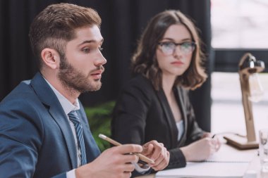 selective focus of young businessman talking at business meeting while sitting near attentive businesswoman