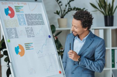 positive african american businessman looking at flipchart with infographics 