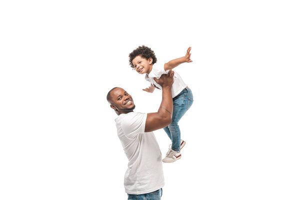 happy african american man holding adorable son above head and smiling at camera isolated on white