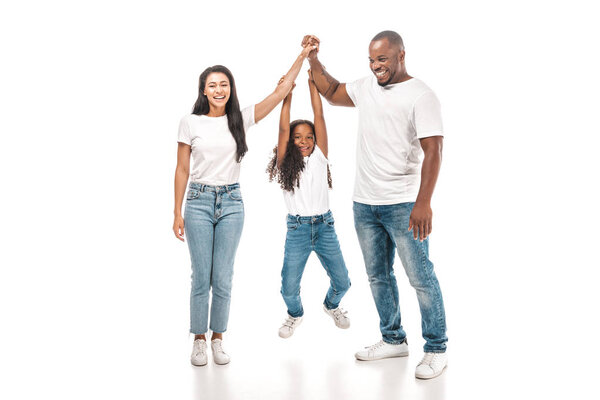 cheerful african american child hanging on hands of parents on white background