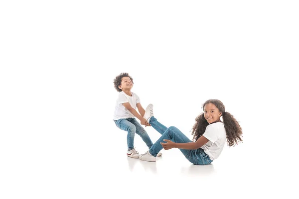 喜びに満ちたアフリカ系アメリカ人の少年が白い背景に足で妹をドラッグ — ストック写真