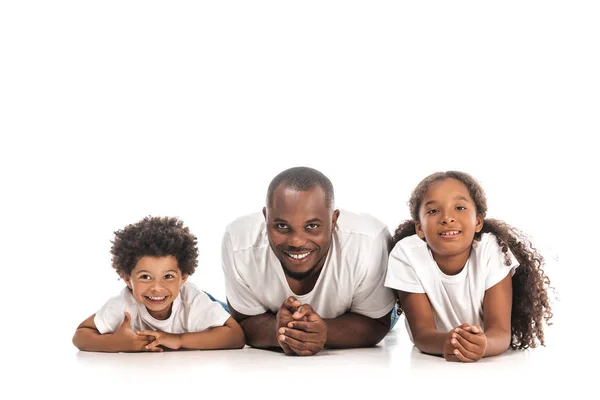 幸せなアフリカ系アメリカ人の父親と息子と娘は白い背景に横になりながらカメラで笑っています — ストック写真