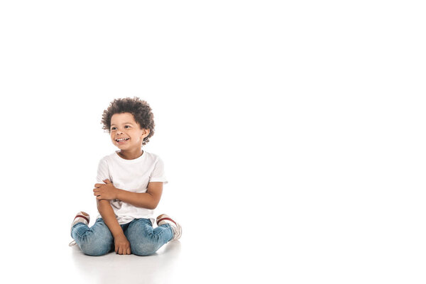 cheerful african american boy looking away while sitting on white background